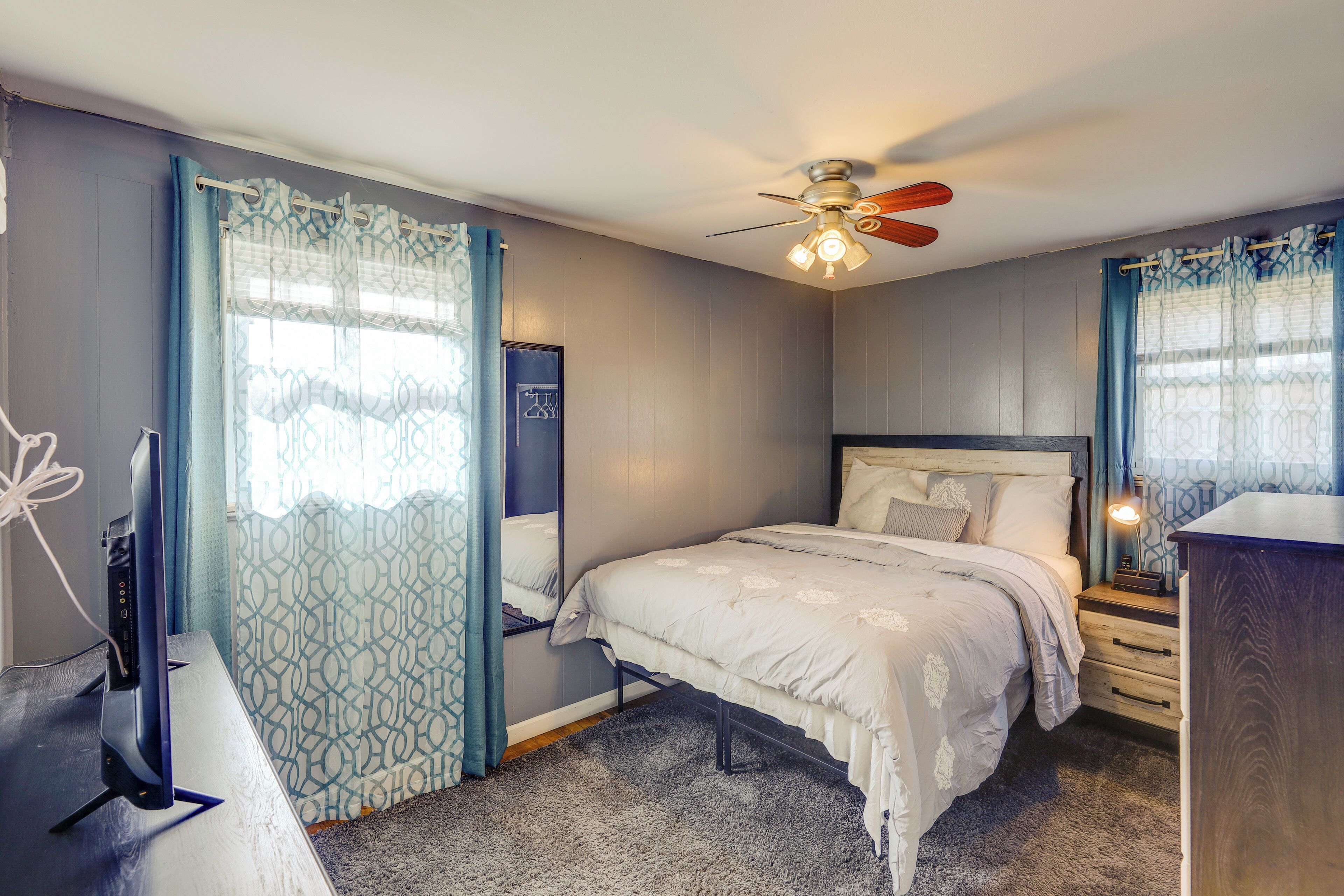 A bedroom with a bed, a ceiling fan, a bedside table with a lamp, and a dresser.
