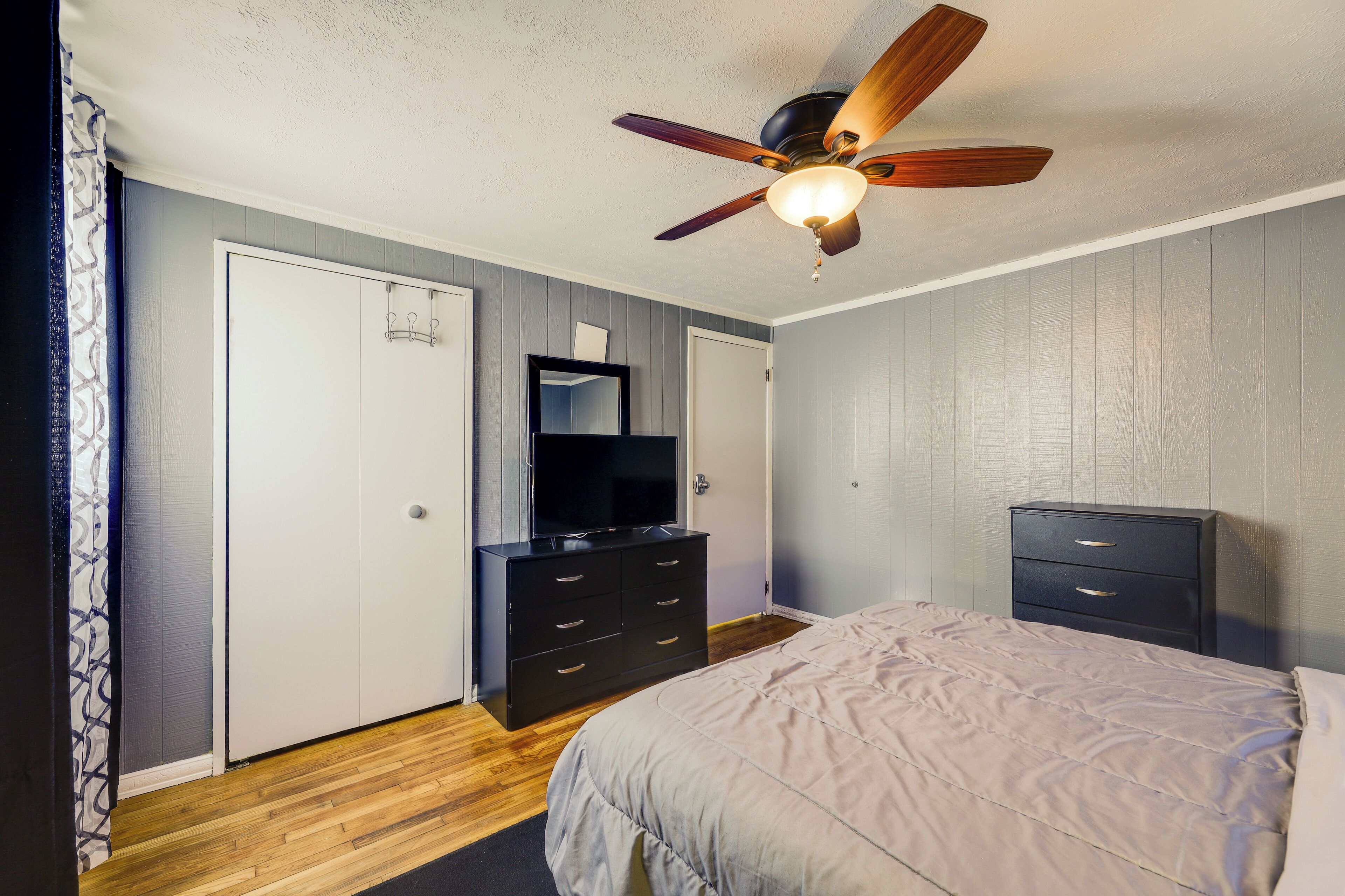 Une chambre à coucher comprenant un lit, une commode, un téléviseur et un ventilateur de plafond.