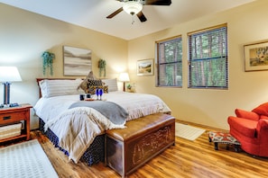 A bedroom with a bed, bedside tables, a red armchair, a ceiling fan, and a window with blinds.