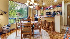 A cozy kitchen with wooden cabinets, a dining area with a round table and chairs, and a large window with blinds. - Fireside Comfort & Family Fun: Wooded Show Low Gem (Show Low)