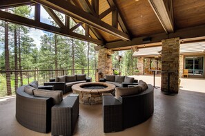 A covered outdoor seating area with a stone fire pit, wicker furniture, and a view of the surrounding forest. - Fireside Comfort & Family Fun: Wooded Show Low Gem (Show Low)