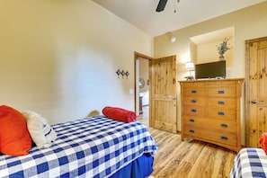 A bedroom with a checkered bedspread, a wooden dresser with multiple drawers, and a television on top. - Fireside Comfort & Family Fun: Wooded Show Low Gem (Show Low)