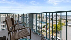A balcony with wicker chairs and a table, overlooking a residential area with houses and a clear sky. - Avalon 507 3 Bedroom Condo by RedAwning (Ocean City)