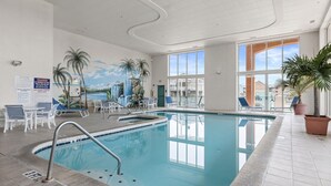 An indoor swimming pool with clear blue water, surrounded by lounge chairs and palm trees. - Avalon 507 3 Bedroom Condo by RedAwning (Ocean City)