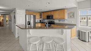 A modern kitchen with a central island, wooden cabinets, stainless steel appliances, and a large window. - Avalon 507 3 Bedroom Condo by RedAwning (Ocean City)