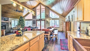 A spacious kitchen with wooden cabinets, granite countertops, and a large island. There is a Christmas tree and a fireplace in the background.