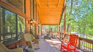 A wooden deck with wicker furniture and a red rocking chair, overlooking a forested area.