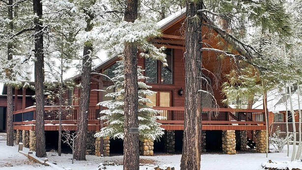 A log cabin with a stone foundation, surrounded by snow-covered trees.