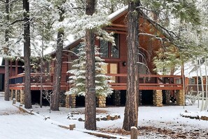 Una cabaña de troncos con cimientos de piedra, rodeada de árboles cubiertos de nieve.
