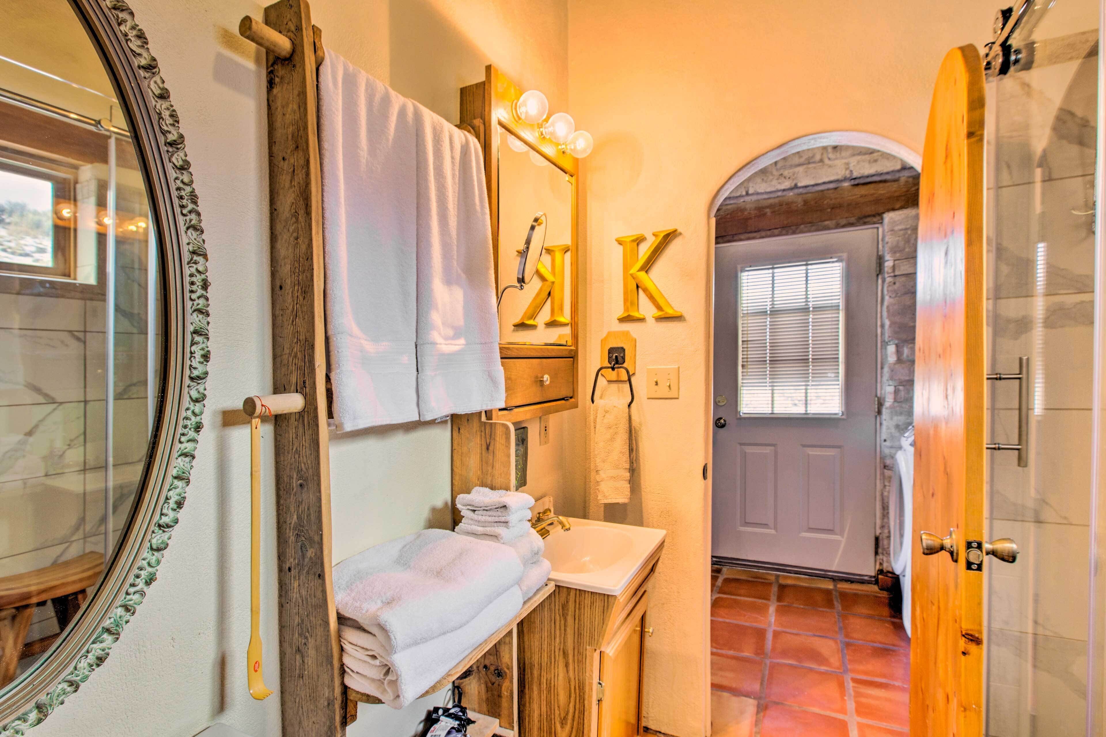 Ein Badezimmer mit einem Holzkosmetikschrank, einem beleuchteten Spiegel, einem Handtuchhalter und einer Tür mit einem 'K'-Schild.