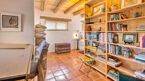 A cozy room with a wooden ceiling, a bookshelf filled with books, a suitcase, and a chair. - Casita Vacation Rental Near Taos w/ Patio! (Taos)