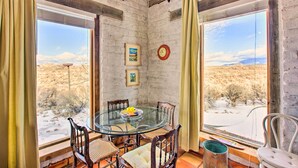 A room with a glass table surrounded by wooden chairs, a clock on the wall, and framed pictures. - Casita Vacation Rental Near Taos w/ Patio! (Taos)