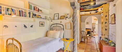 Een knus slaapkamer met een bed, een klein tafeltje en een boekenplank vol boeken.
