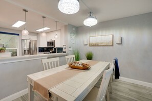 A modern kitchen with stainless steel appliances, pendant lighting, and a dining area with a long table and chairs. - Tranquil Redington Beach Condo w/ Beach Access (Redington Beach)