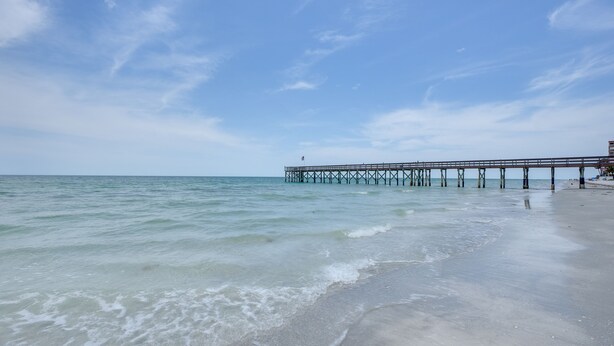 A beach with a pier extending into the ocean. - Tranquil Redington Beach Condo w/ Beach Access (Redington Beach)