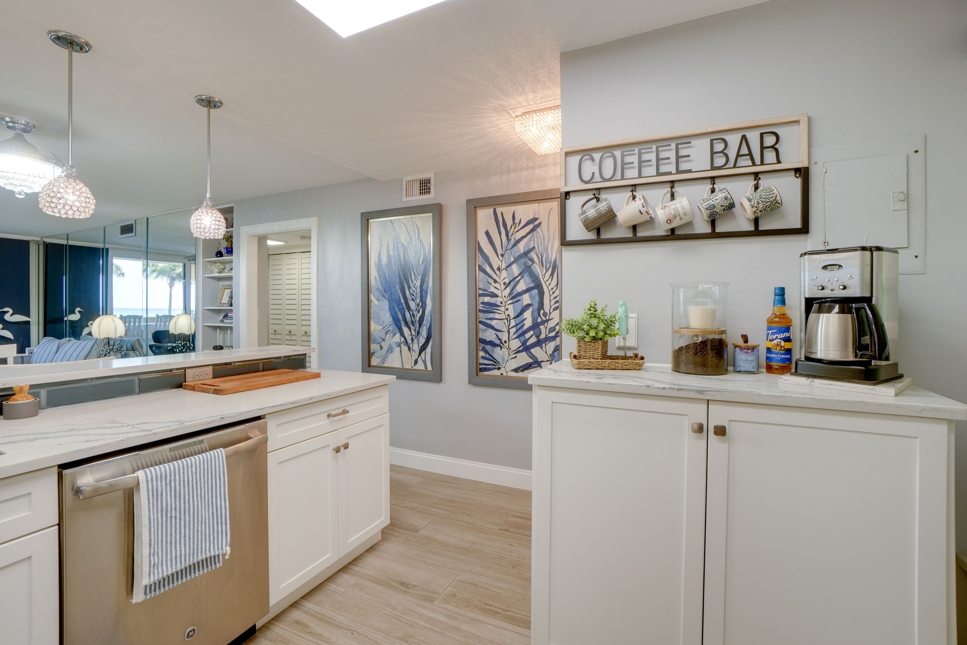 Une cuisine moderne avec des meubles blancs, un coin café agrémenté d’une enseigne et des œuvres d’art décoratives.