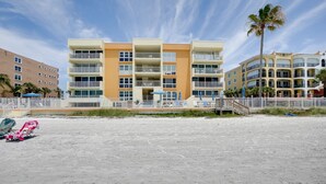 A beachfront hotel with multiple balconies, a sandy beach in the foreground, and palm trees. - Tranquil Redington Beach Condo w/ Beach Access (Redington Beach)