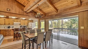 A spacious kitchen with wooden cabinets, a dining area with a large table and chairs, and a balcony with a view of trees. - Ski & Soak: Hot Tub Haven in Tahoe City! (Tahoe City)