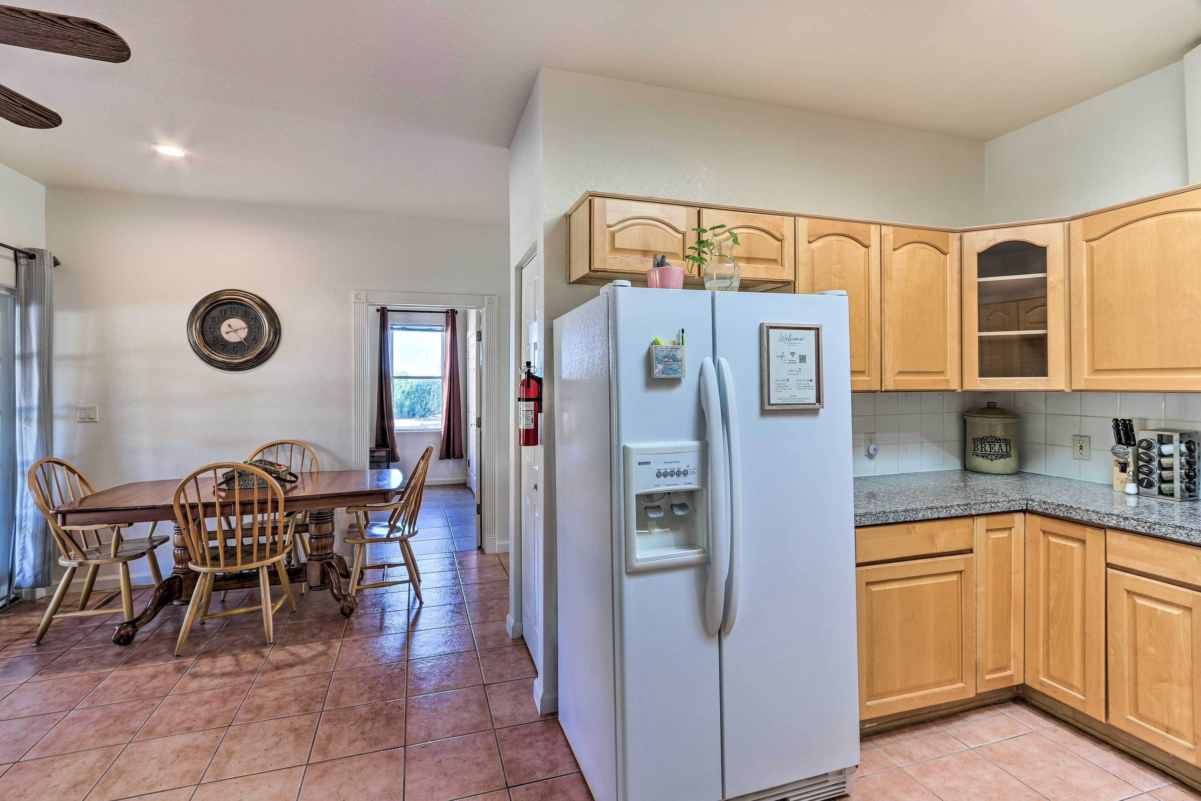 A kitchen with wooden cabinets, a white refrigerator, a dining table with chairs, and a tiled floor.