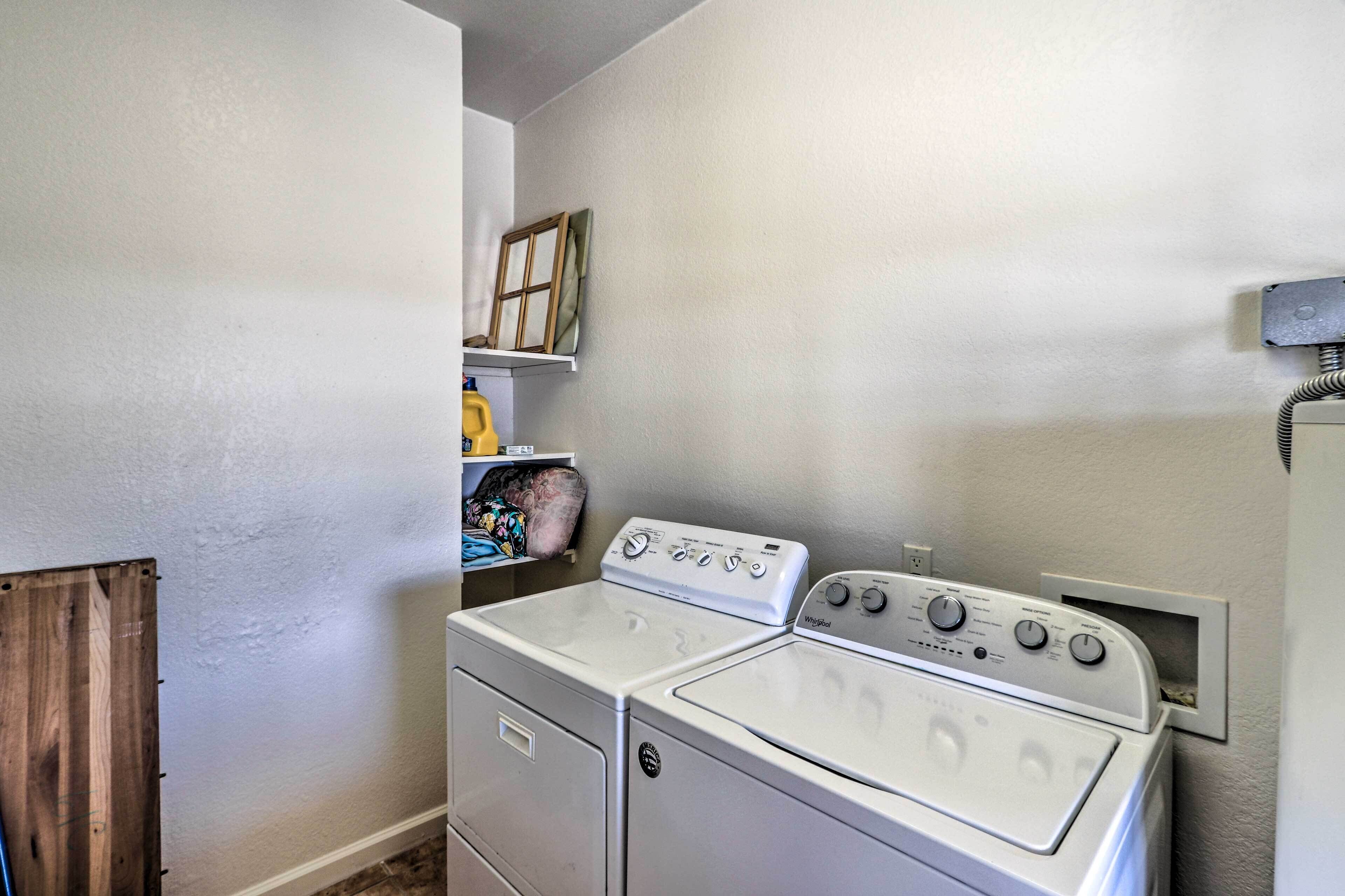 A laundry room with a front-loading washer and dryer, a shelf with a yellow bottle, and a wooden door.