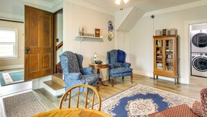 A living room with a staircase, two patterned armchairs, a wooden cabinet, and a washing machine. - Peaceful Country Home in Serene Setting With Yard (Washington)
