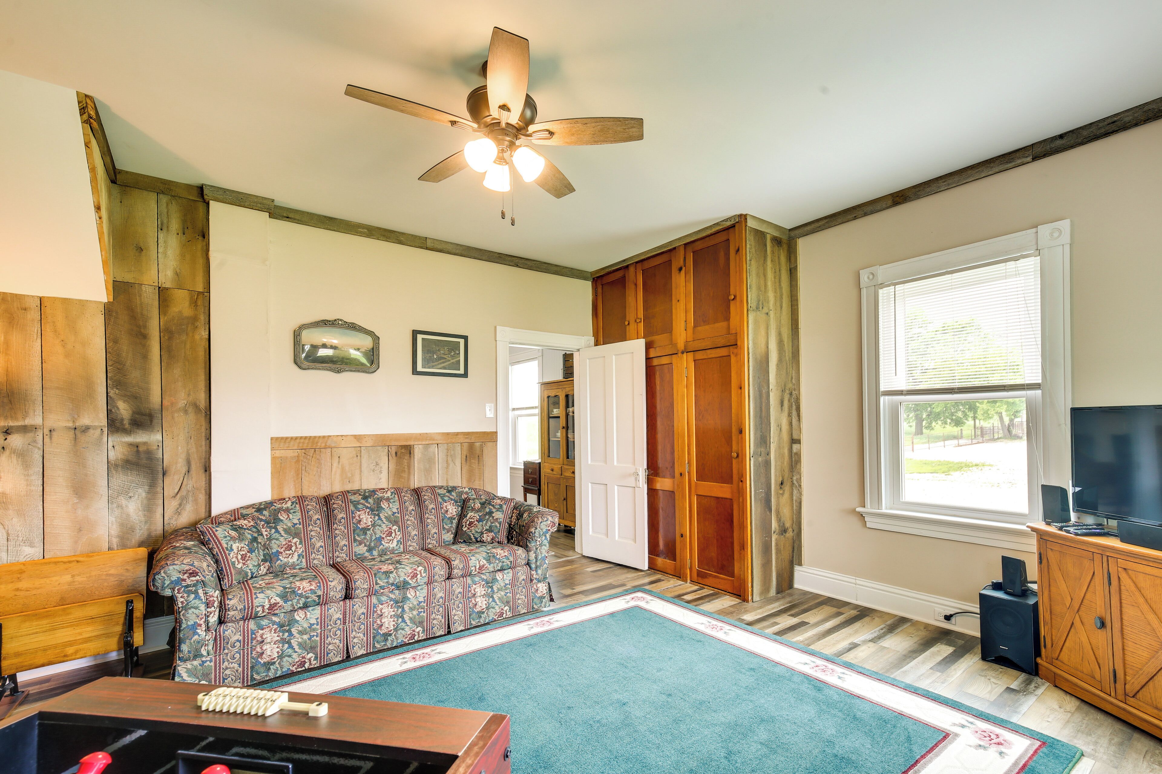 A living room with a patterned sofa, wooden cabinets, a ceiling fan, and a large window.