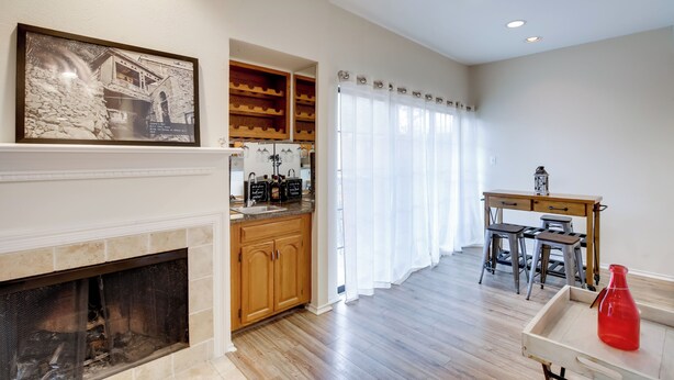 A modern living room with a fireplace, wooden cabinets, a dining area with a table and chairs, and a large window with curtains. - Comfortable Dallas Condo Close to Attractions (Dallas)