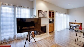 A spacious living room with a fireplace, a flat-screen TV on a stand, wooden flooring, and a dining area with a table and chairs. - Comfortable Dallas Condo Close to Attractions (Dallas)