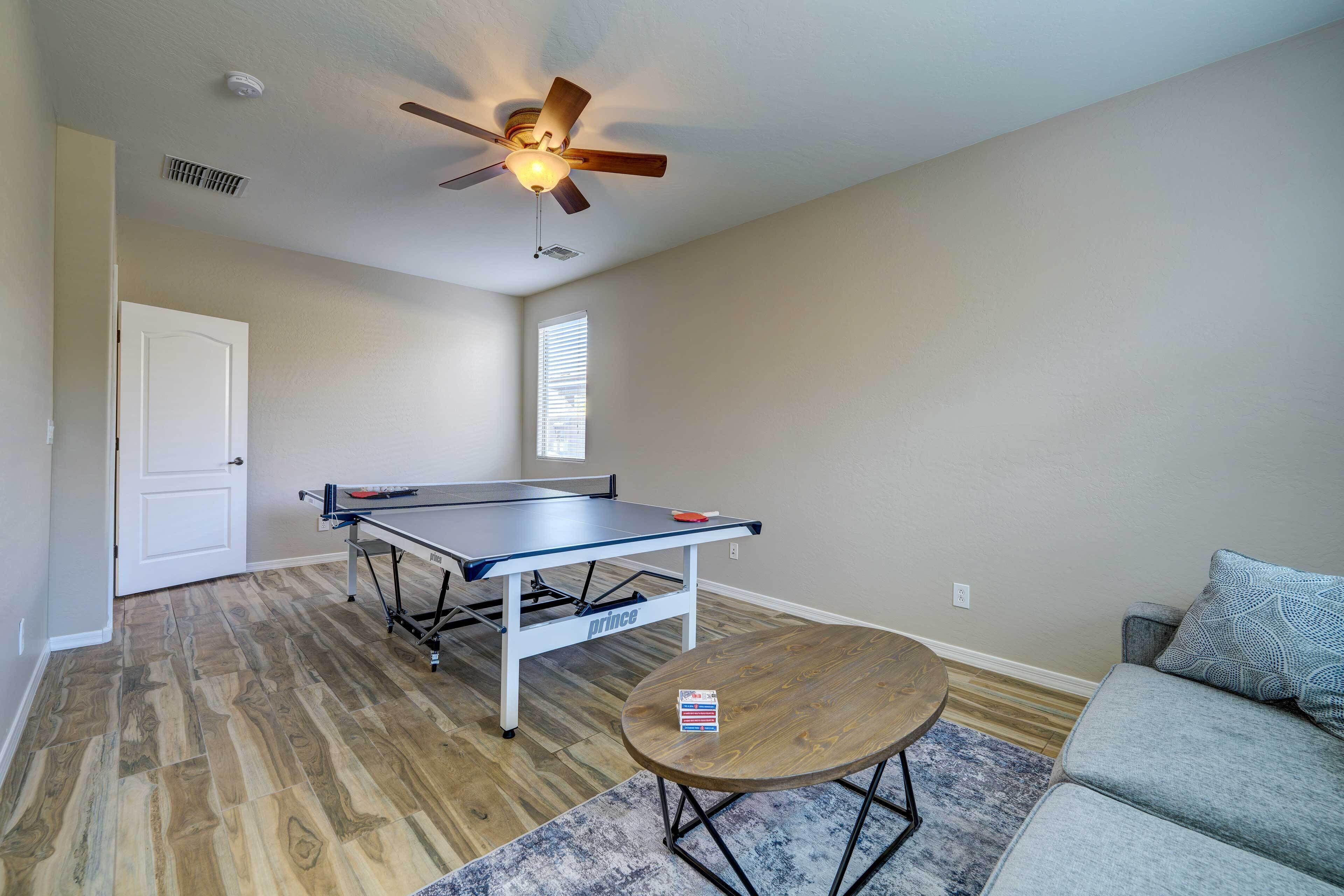 A room with a ping pong table, a ceiling fan, a door, and a gray sofa.