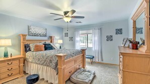 Um quarto com cama de madeira, ventoinha no teto, janela com cortinas e cômoda.