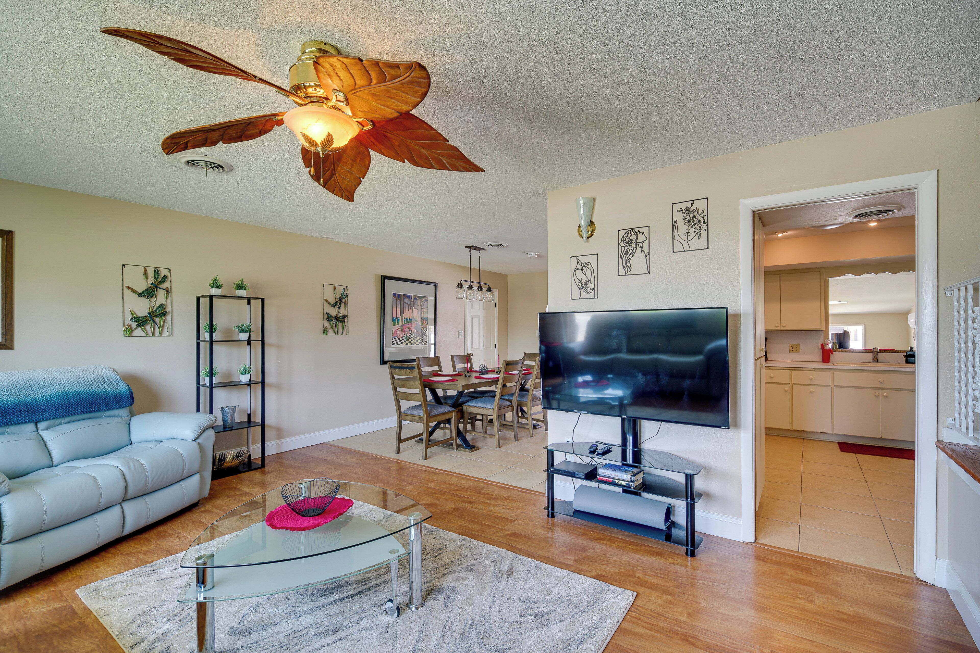 A living room with a sofa, a glass coffee table, a TV, and a ceiling fan.