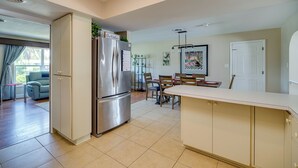 Una cocina moderna con un refrigerador empotrado, un comedor con mesa y sillas, y una sala de estar con sofá y ventana.