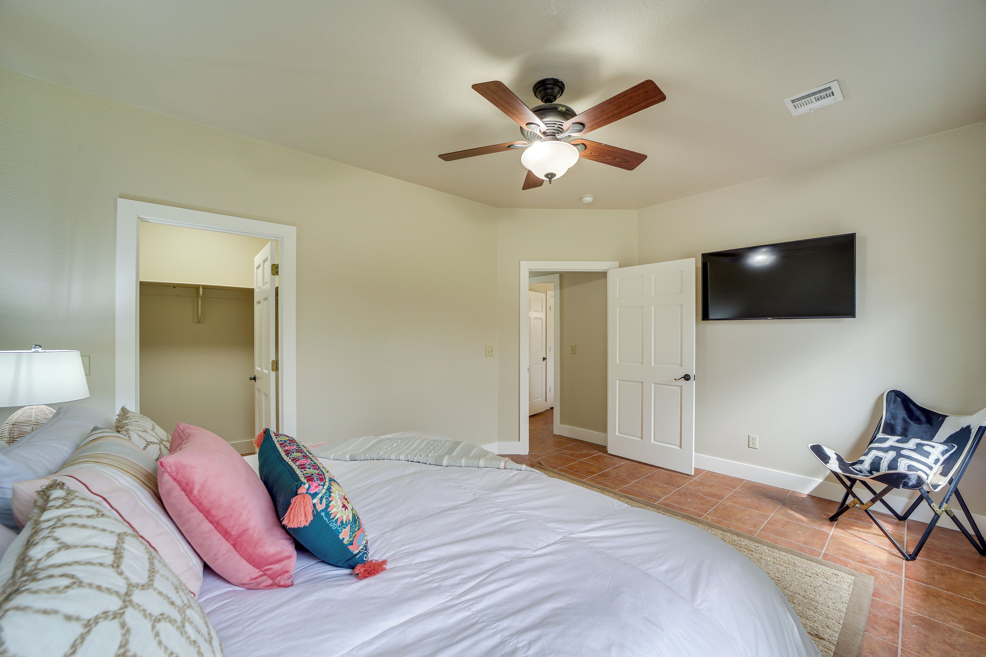 A bedroom with a bed, pillows, a ceiling fan, a TV, and a chair.