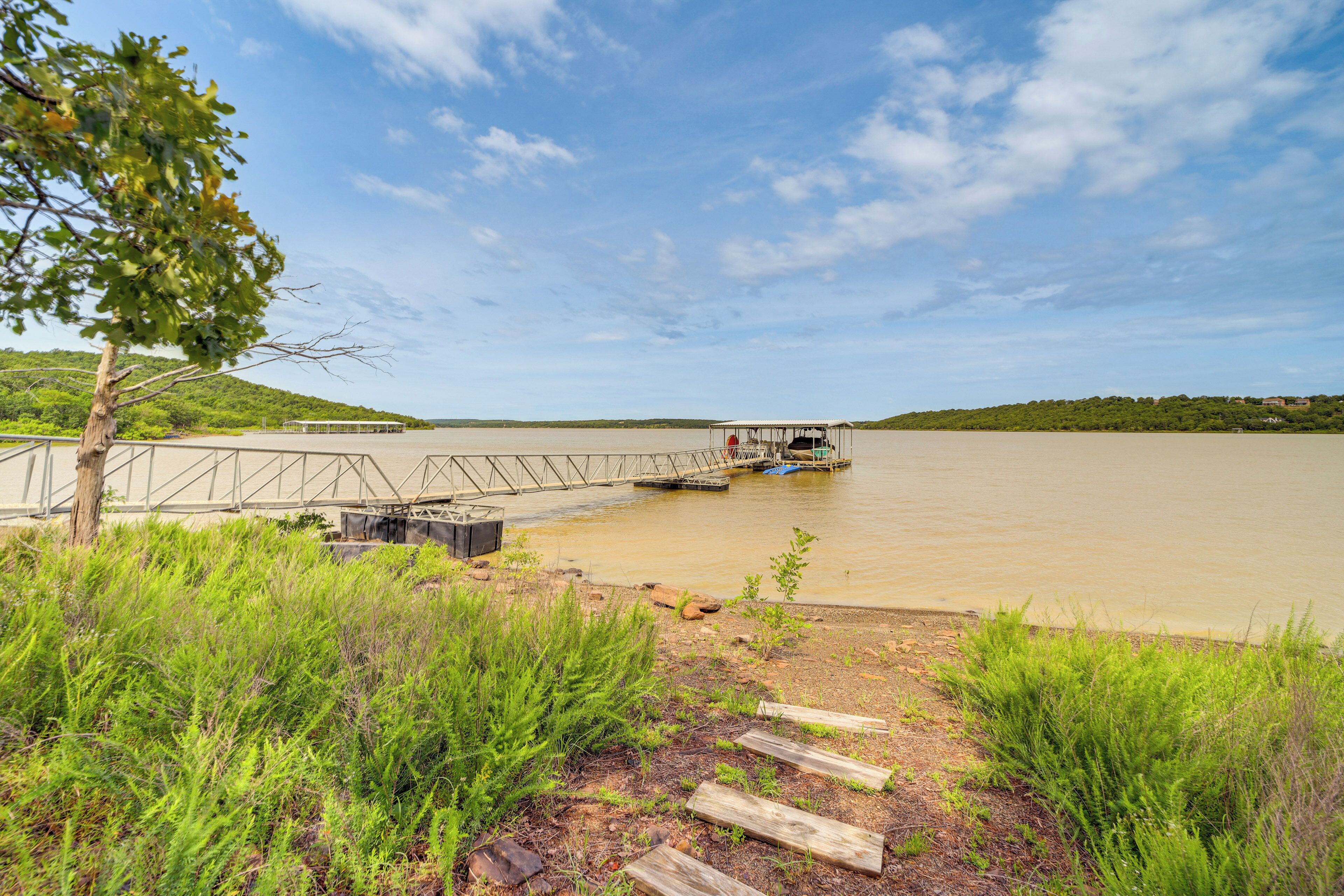 Un muelle a la orilla del río con un barco pequeño, rodeado de vegetación y un cielo despejado.