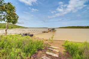 A riverside dock with a small boat, surrounded by greenery and a clear sky. - Lakefront Eufaula Vacation Rental w/ Private Dock (Eufaula)