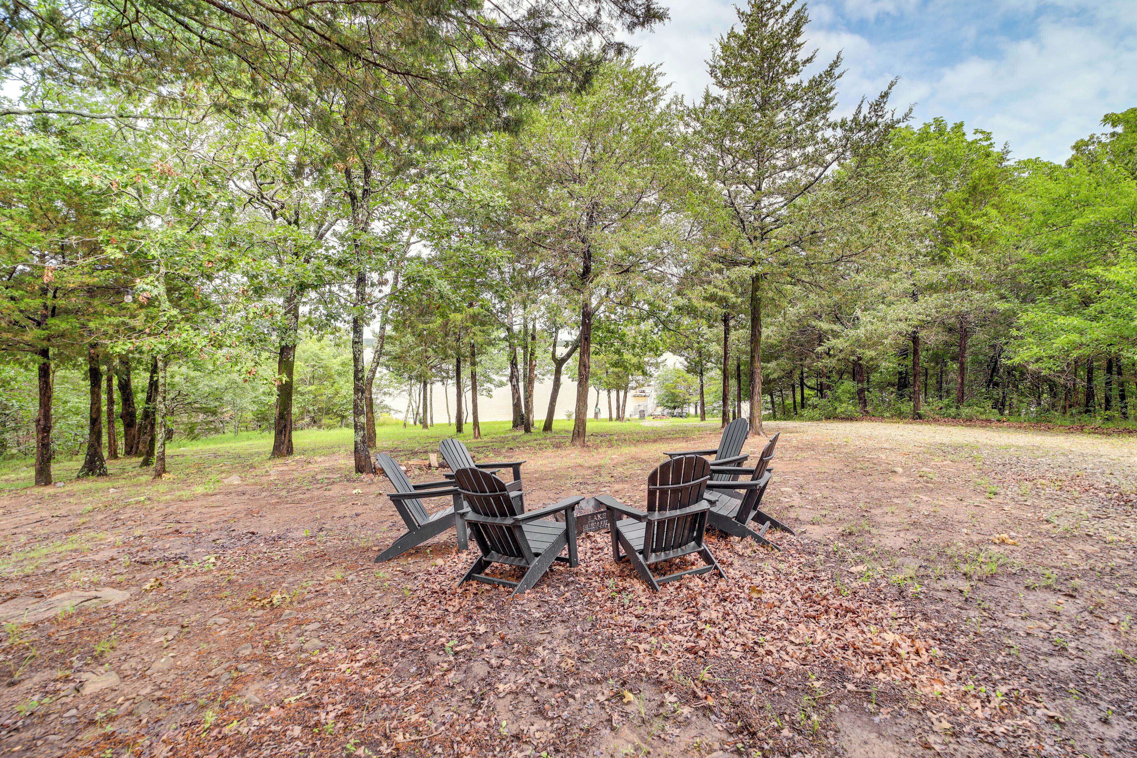 A forested area with two Adirondack chairs facing each other on a dirt ground.
