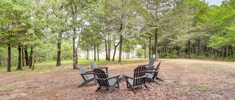 A forested area with two Adirondack chairs facing each other on a dirt ground.