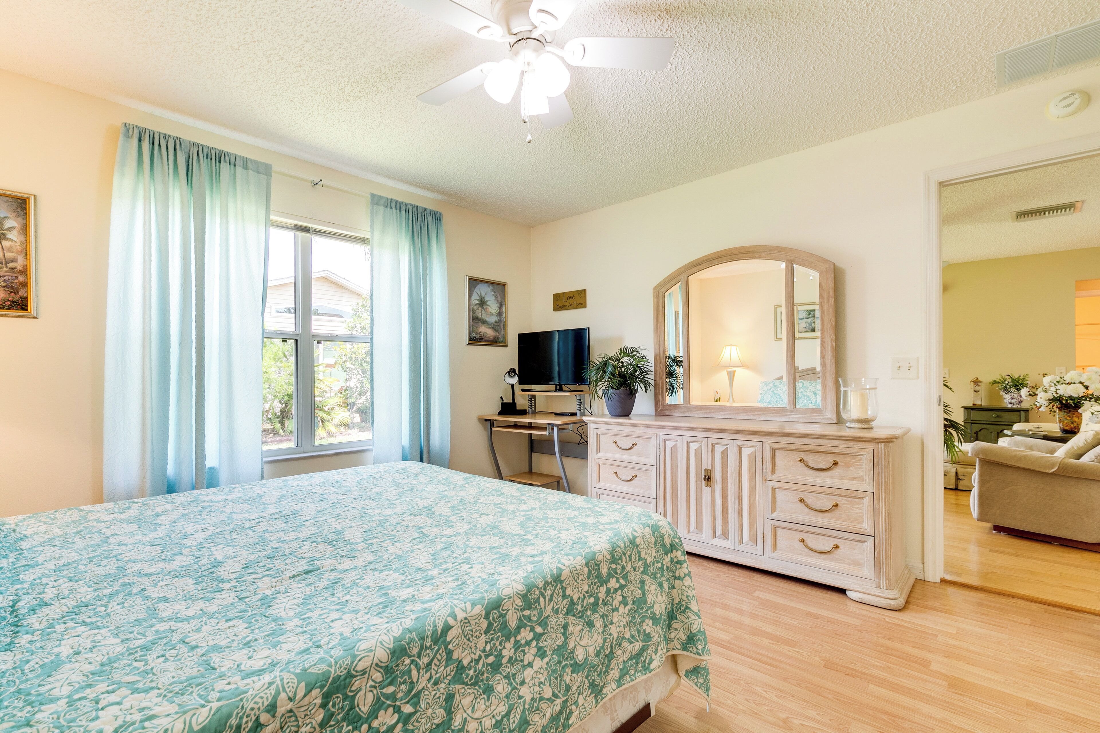 A bedroom with a bed, a desk, a dresser, a mirror, and a window with curtains.