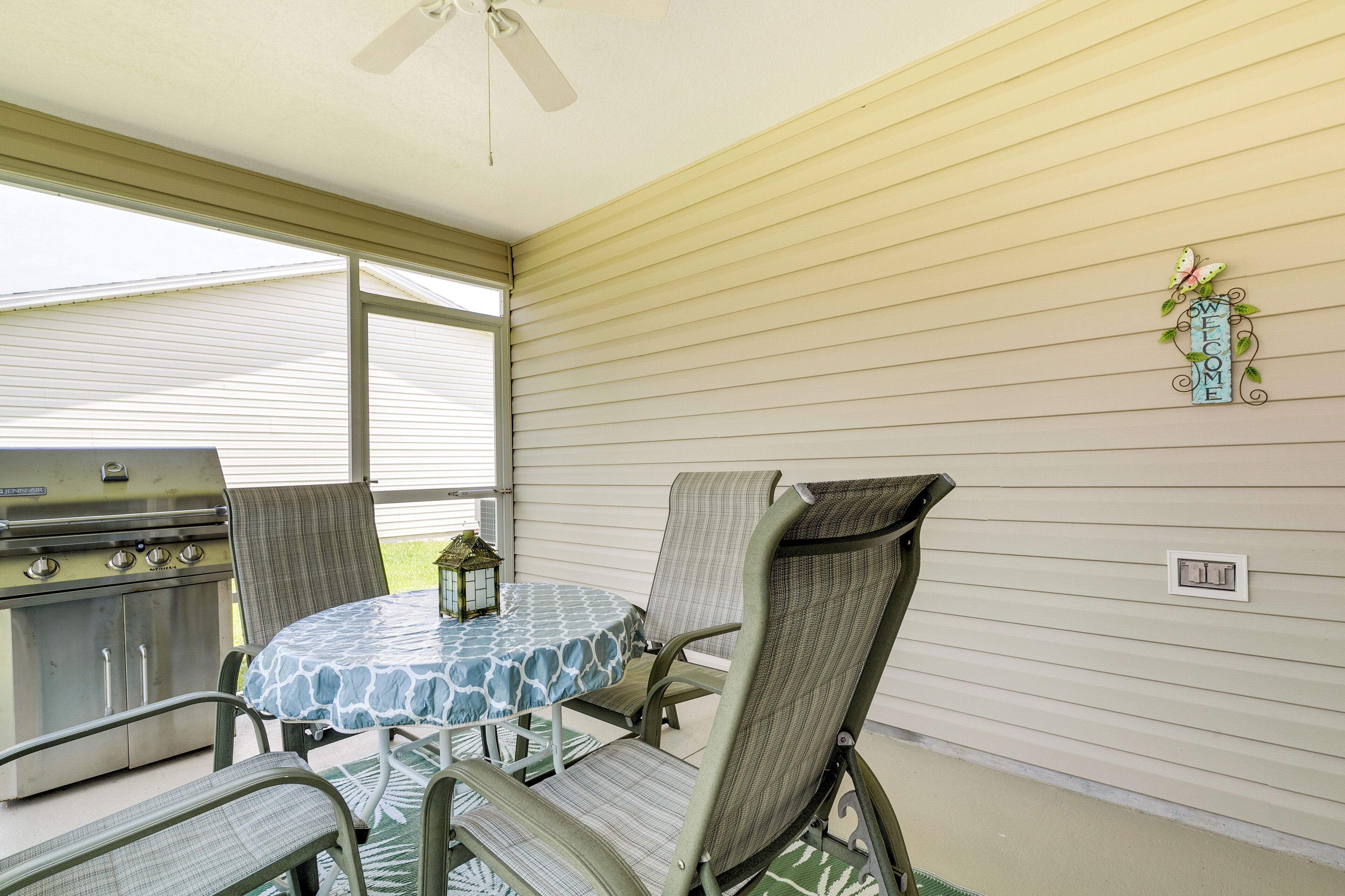An outdoor patio with a round table and chairs, a grill, and a welcome sign.