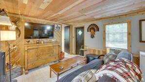 A cozy cabin interior with a wooden ceiling, a large TV on a wooden cabinet, a sofa, and a small table. - Hemphill Home w/ Community Perks < 1 Mi to Water! (Hemphill)
