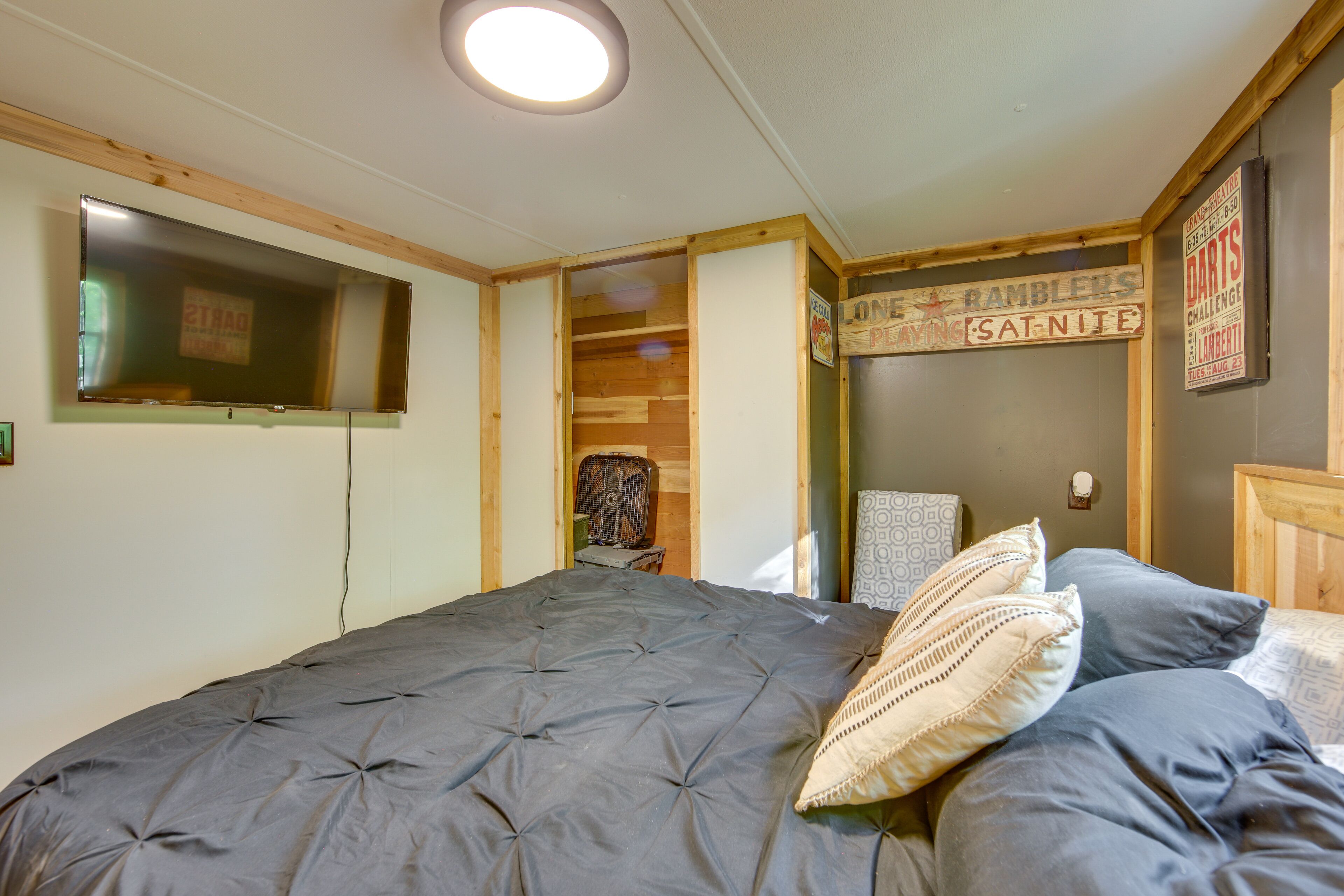 A bedroom with a large bed, a flat-screen TV mounted on the wall, and a wooden ceiling.