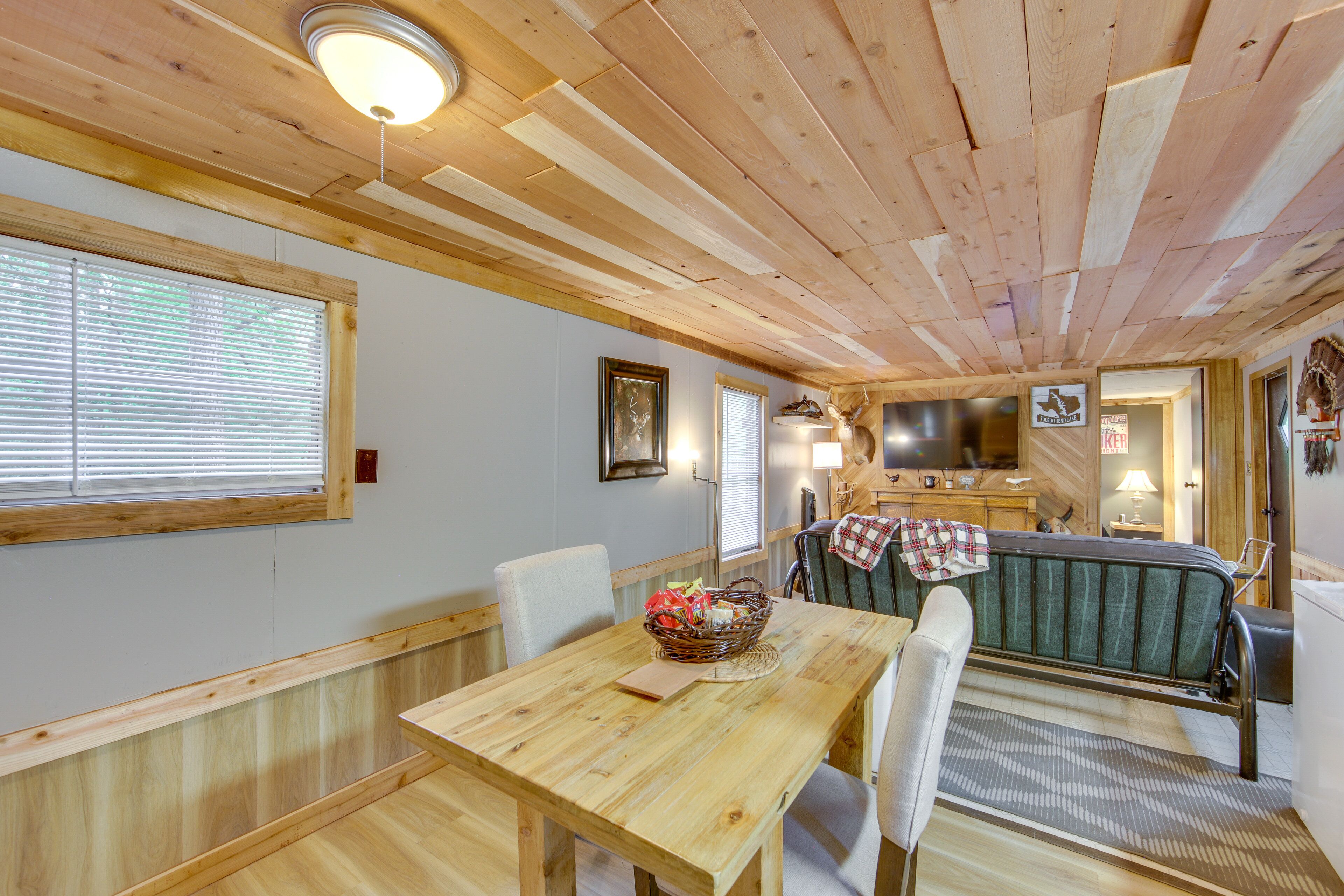 A wooden interior with a dining table, chairs, a sofa, and a television.