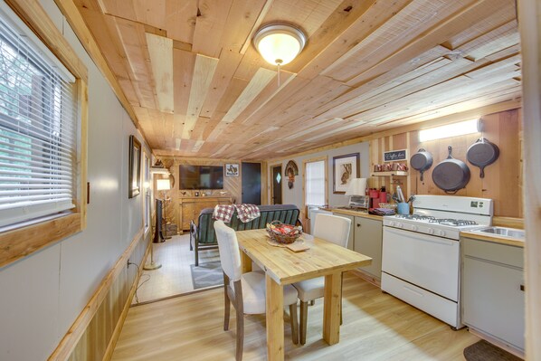 Une cuisine chaleureuse avec des poutres en bois, une table à manger, des chaises, un poêle et un réfrigérateur.