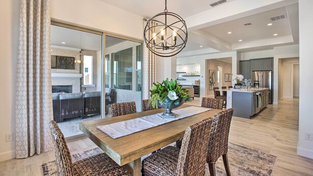 A dining area with a wooden table, woven chairs, and a hanging light fixture. - Luxury Spring Training Home Base in Goodyear! (Goodyear)