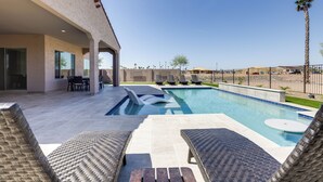 A swimming pool with lounge chairs, a covered patio area, and a view of the surrounding landscape. - Luxury Spring Training Home Base in Goodyear! (Goodyear)