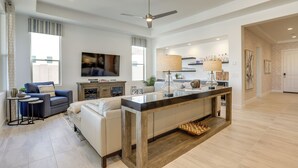A spacious living area with a central island, a sofa, a TV, and a kitchen area with a bar. - Luxury Spring Training Home Base in Goodyear! (Goodyear)