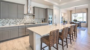 A modern kitchen with grey cabinets, a tiled backsplash, and a central island with bar stools. - Luxury Spring Training Home Base in Goodyear! (Goodyear)