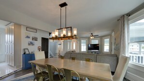 Een ruime woonkamer met een grote houten eettafel, comfortabele zithoek, een inbouwtelevisie meubel en uitzicht op de stad door grote ramen.