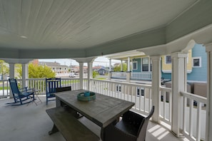 A covered patio with a wooden table and blue chairs, white railings, and a view of a street with houses.