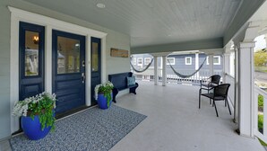 Een overdekte veranda met een bank, stoelen en potplanten.